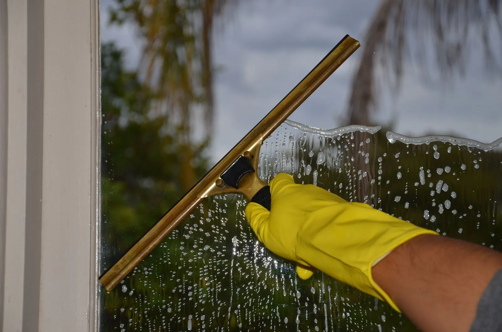 A squeegee clearing soapy water from a home window, leaving spot free glass